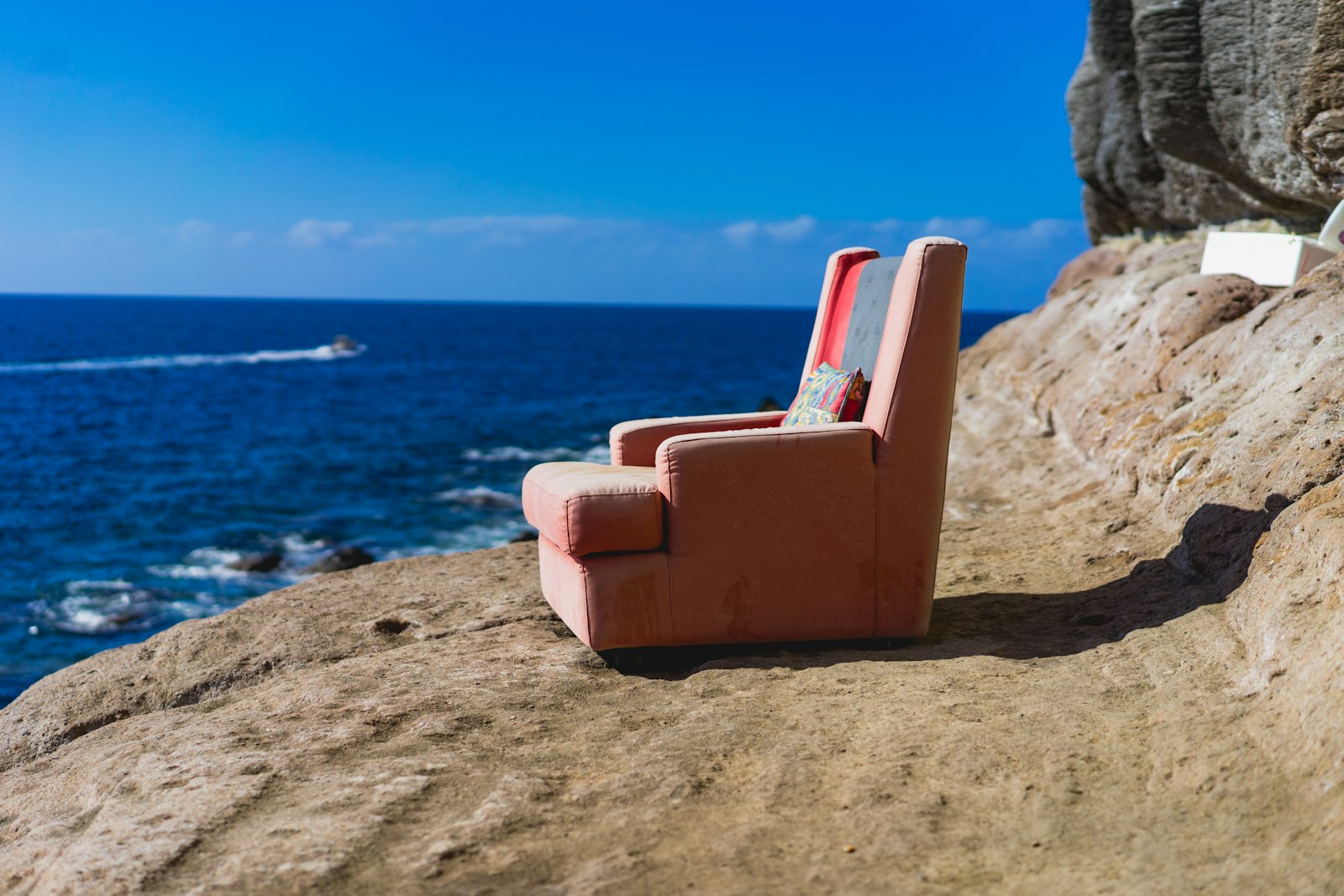 Worn pink armchair on a rocky cliff above a deep blue sea
