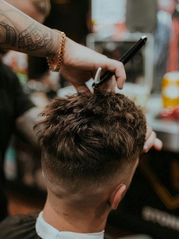 Barber running clippers over a young man's head, product bottles blurred behind