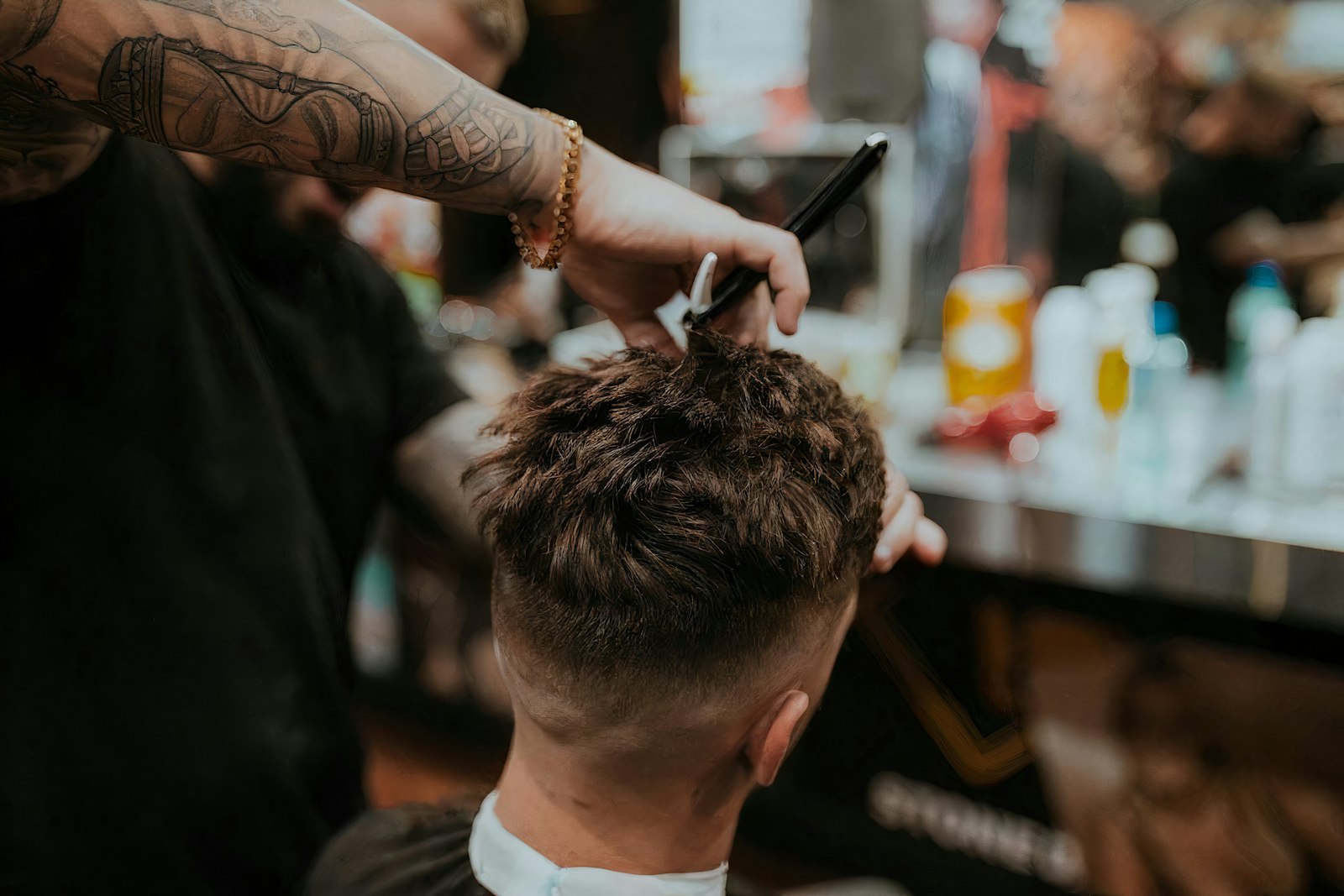 Barber running clippers over a young man's head, product bottles blurred behind