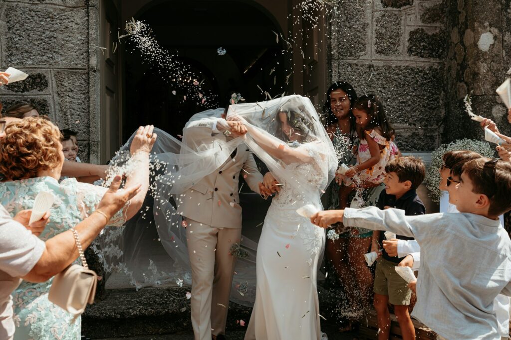 Newlyweds leaving a stone chapel doorway in a shower of confetti