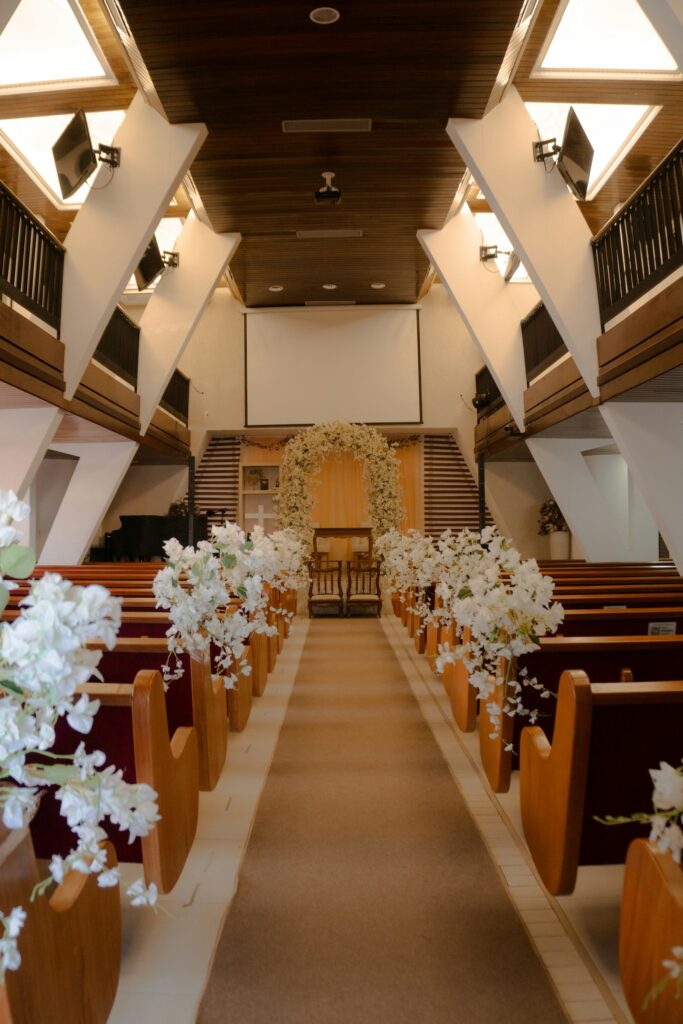 White floral arrangements lining the pew ends of a church aisle