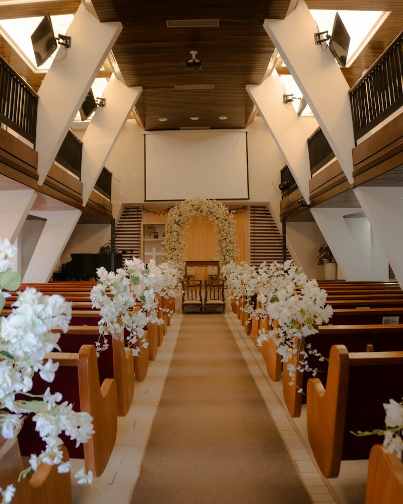 White floral arrangements lining the pew ends of a church aisle