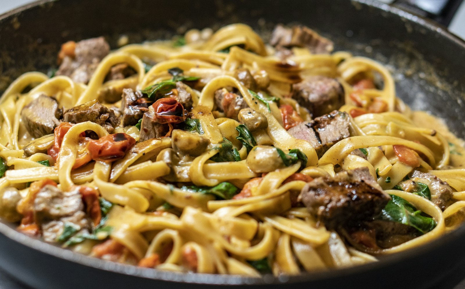 Creamy fettuccine with beef and tomatoes in a pan