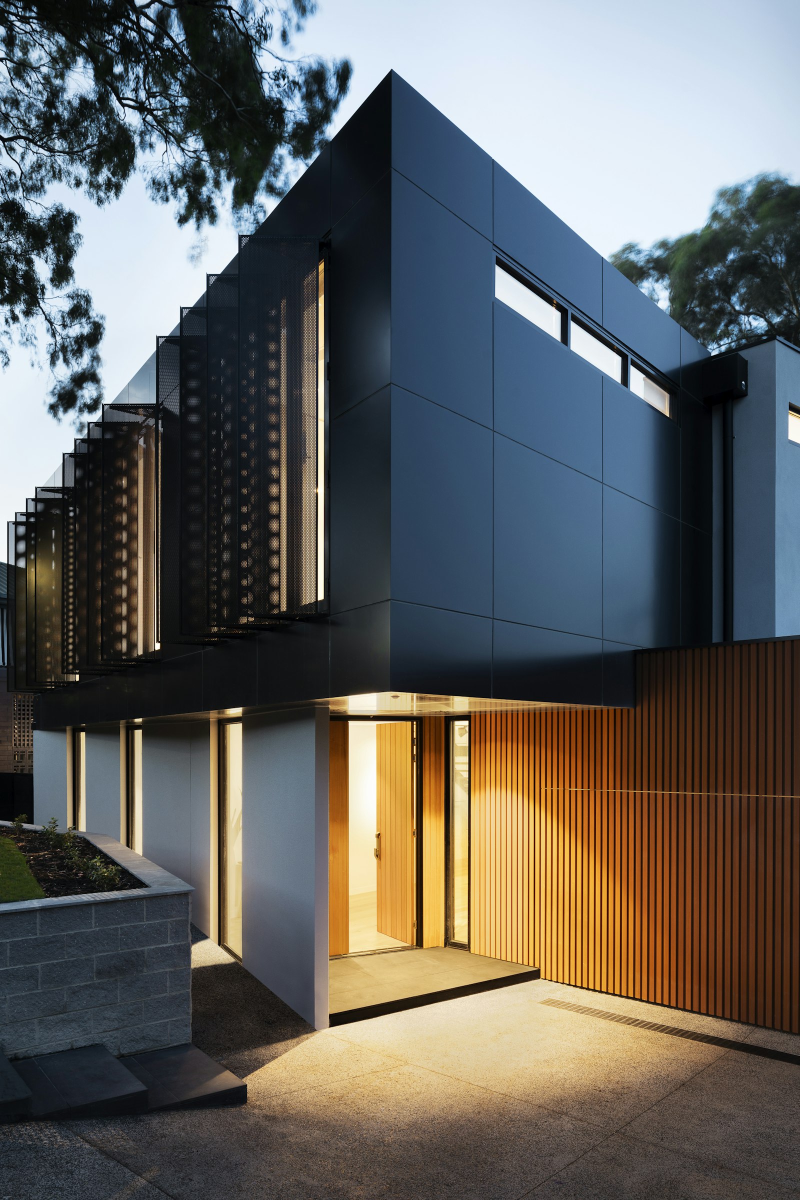 Dark clad modern house with lit timber entry