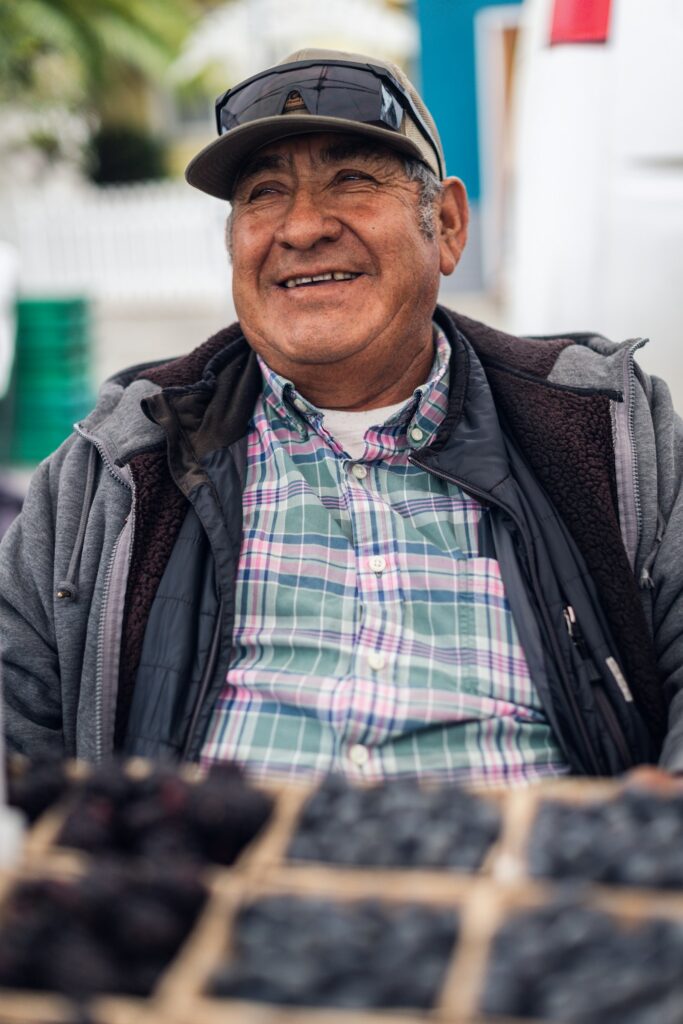 Smiling farmer in a cap and plaid shirt behind crates of berries