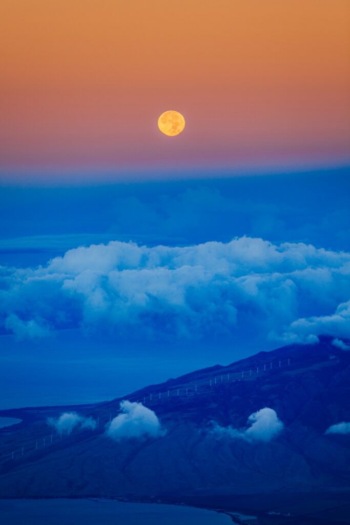 Full moon rising above clouds and mountain ridge