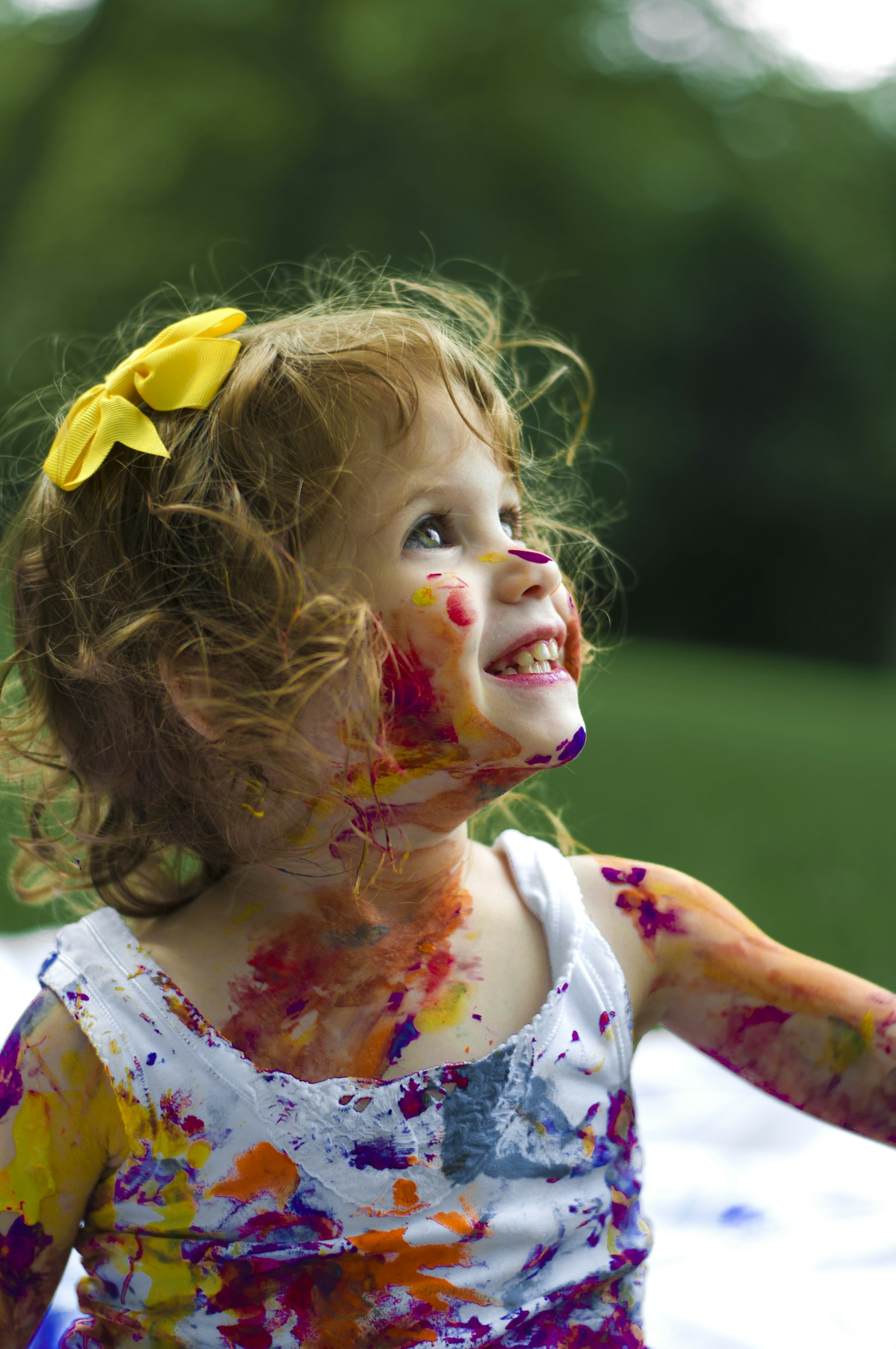 Smiling toddler with a yellow hair bow and paint smeared on her face and dress