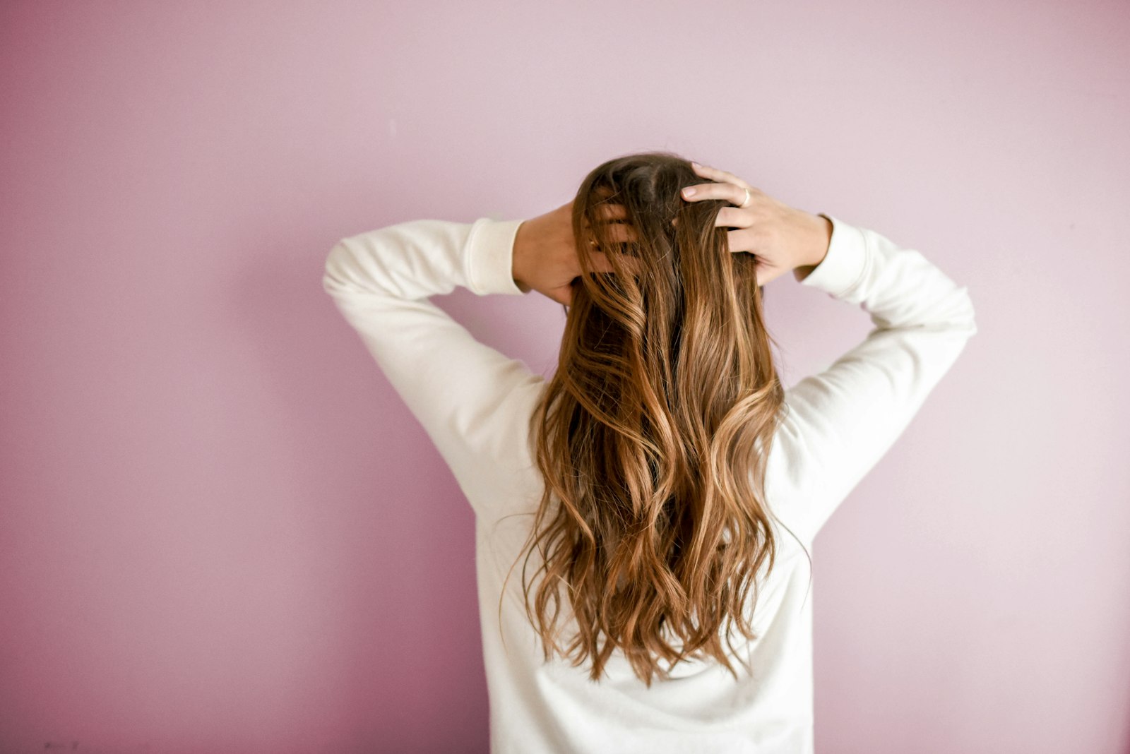 Woman with long wavy hair seen from behind on a pink backdrop