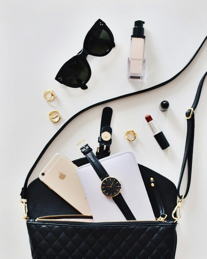 Flatlay of a black handbag with sunglasses and lipstick