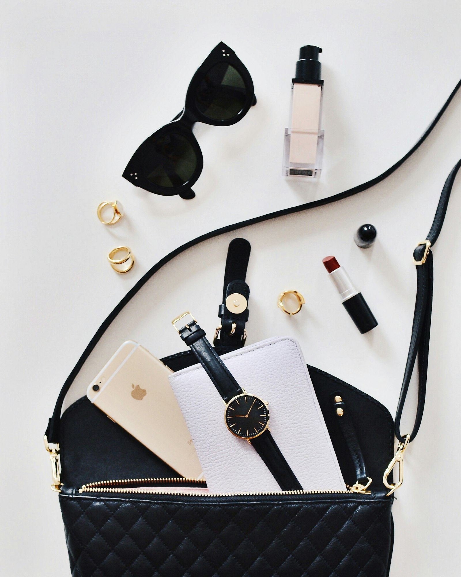 Flatlay of a black handbag with sunglasses and lipstick