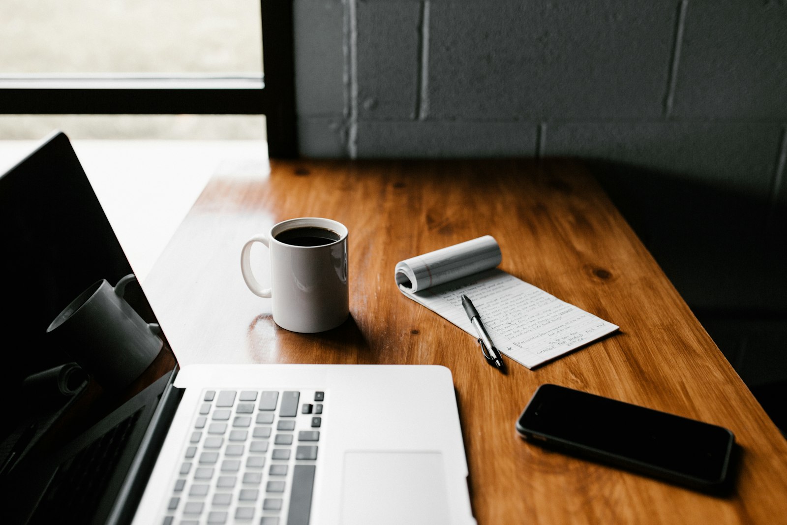 Laptop, coffee mug and notebook on a wooden desk