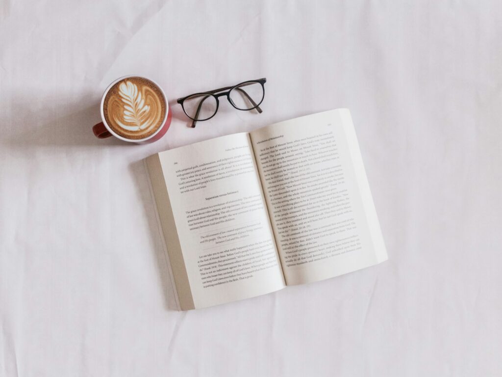 Open book, latte and glasses on white linen