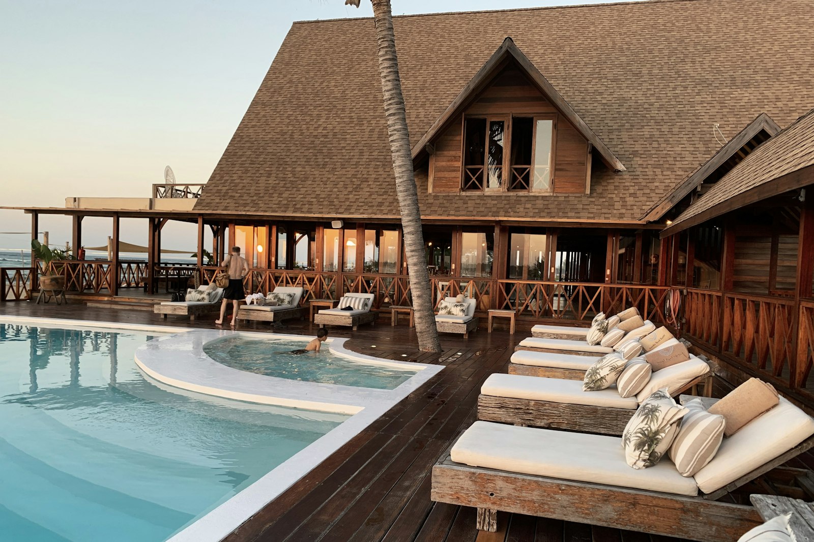 Thatched resort lodge with sun loungers along a timber pool deck at golden hour