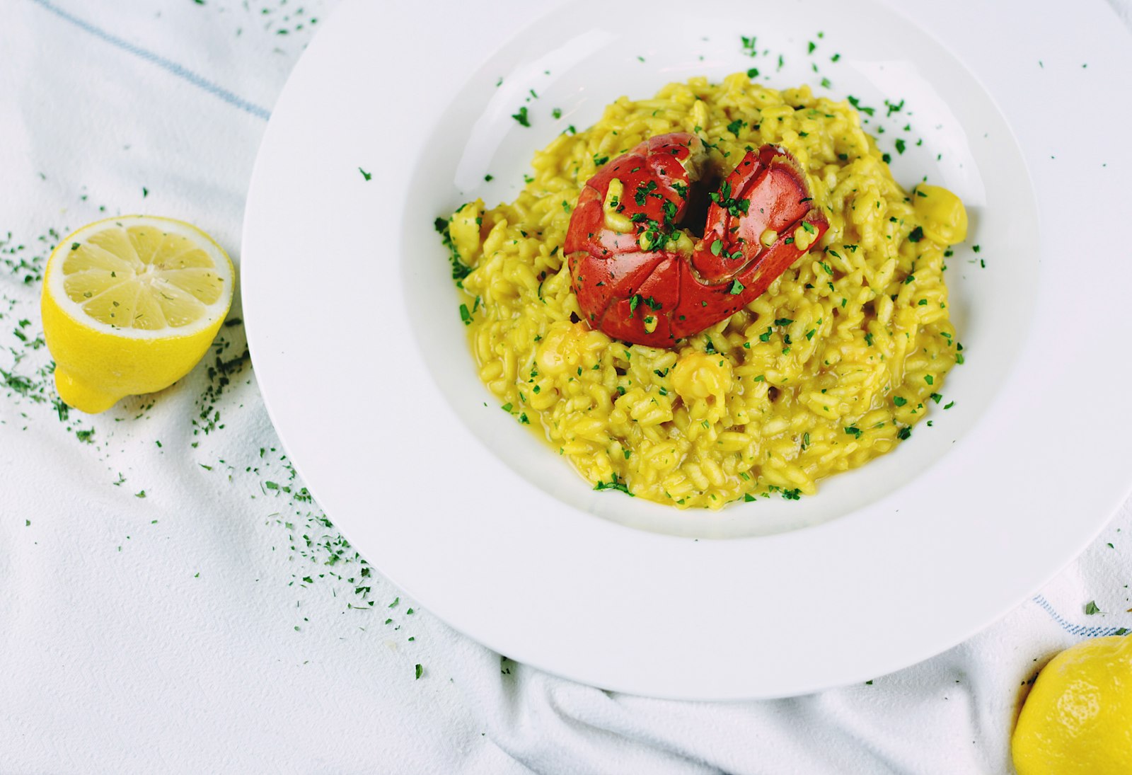 Saffron risotto with a roasted tomato in a deep white plate, lemon halves on a linen cloth
