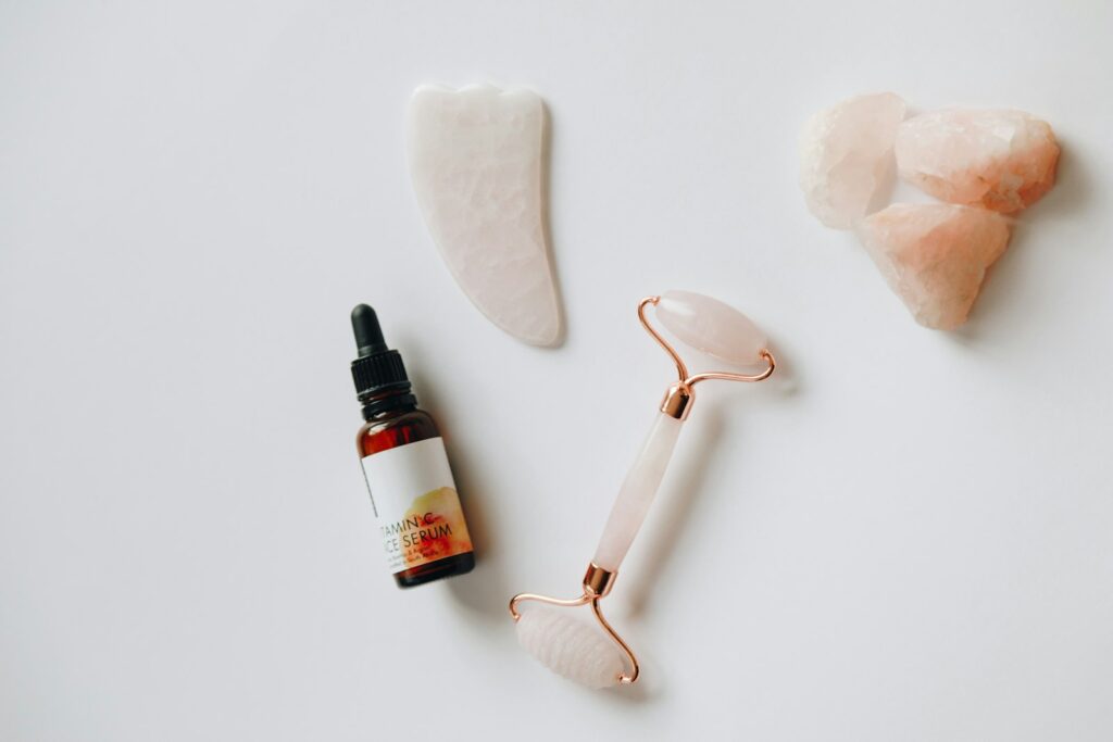 Jade roller, gua sha and serum on a pale surface