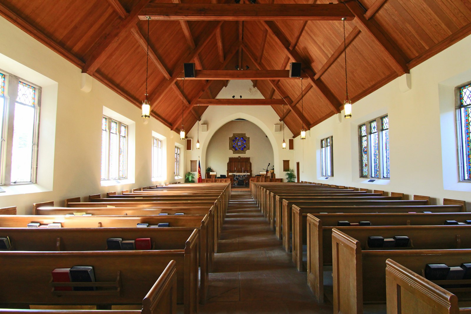 Empty stone chapel with a timber roof and wooden pews either side of the aisle