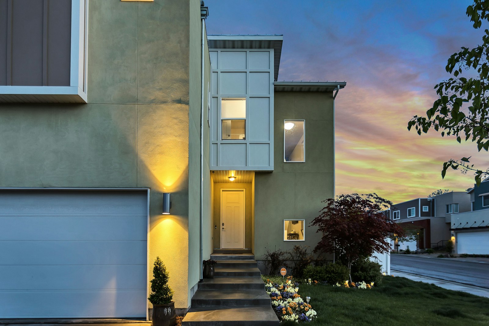 Two-storey stucco house with a lit entry and garage under a pink dusk sky