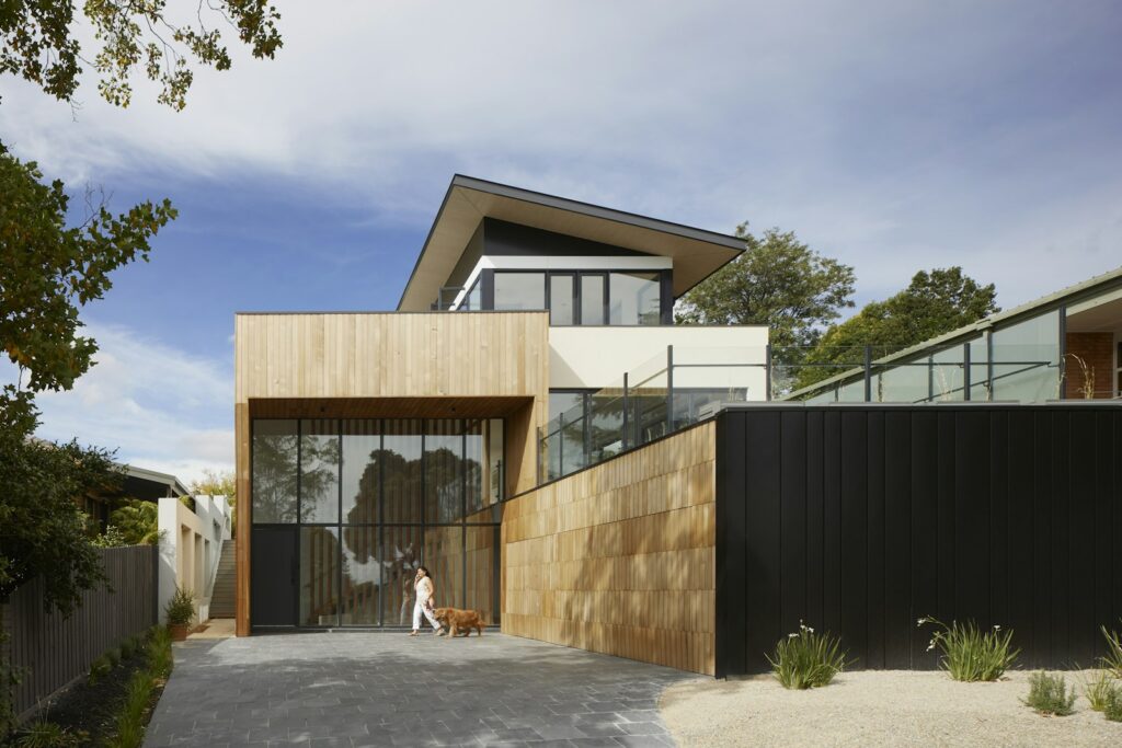 Modern timber and dark-clad house above a concrete driveway on a bright day