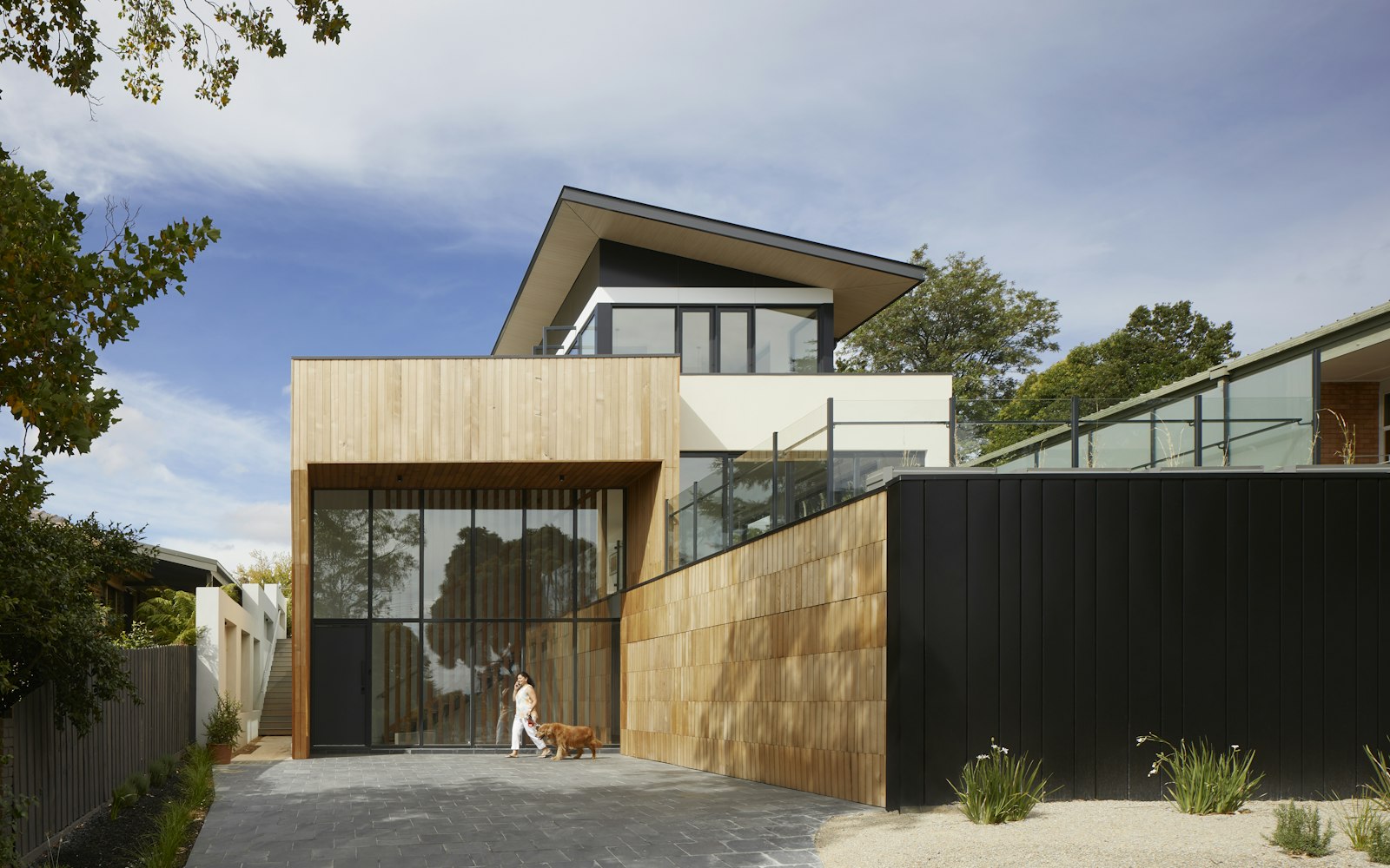 Modern timber and dark-clad house above a concrete driveway on a bright day