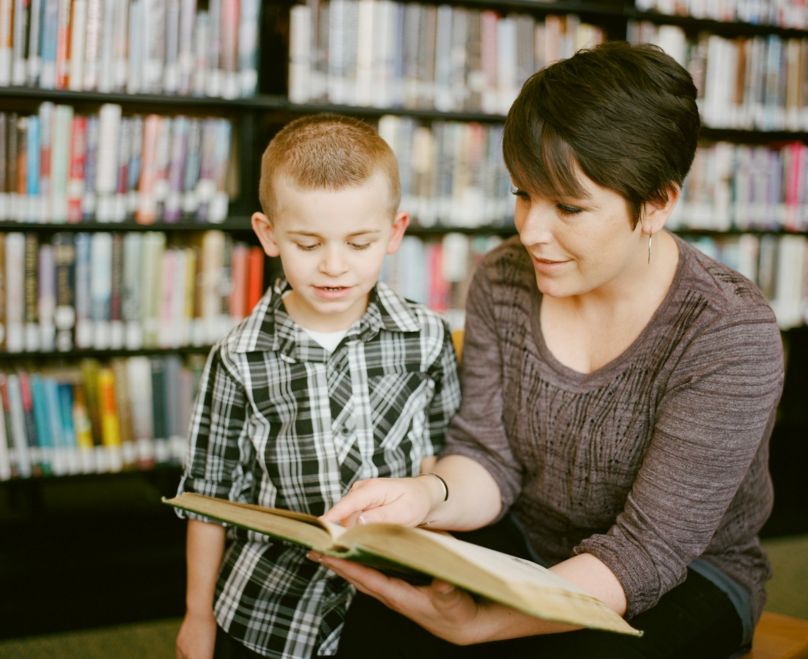Tutor reading a book with a child in the library