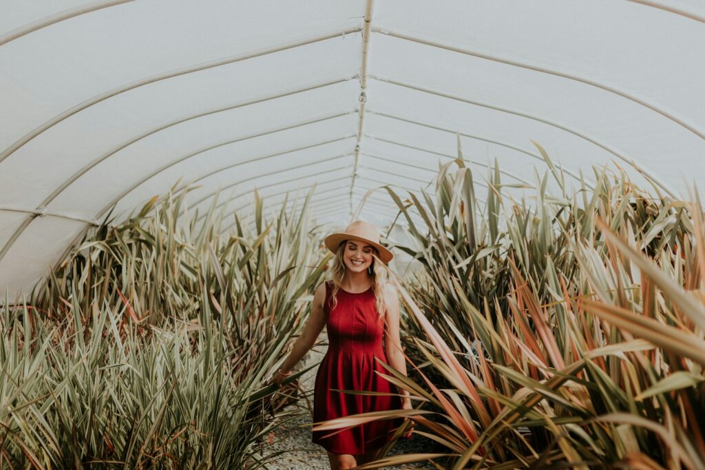 Woman in a red dress and straw hat smiling in a polytunnel of long-leaved plants